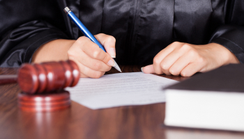 A judge's hand writing on paper with a pen and a gavel